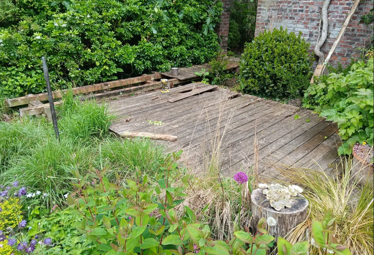 Ancien platelage bois dégradé avant travaux, jardin clos en briques à Rexpoëde